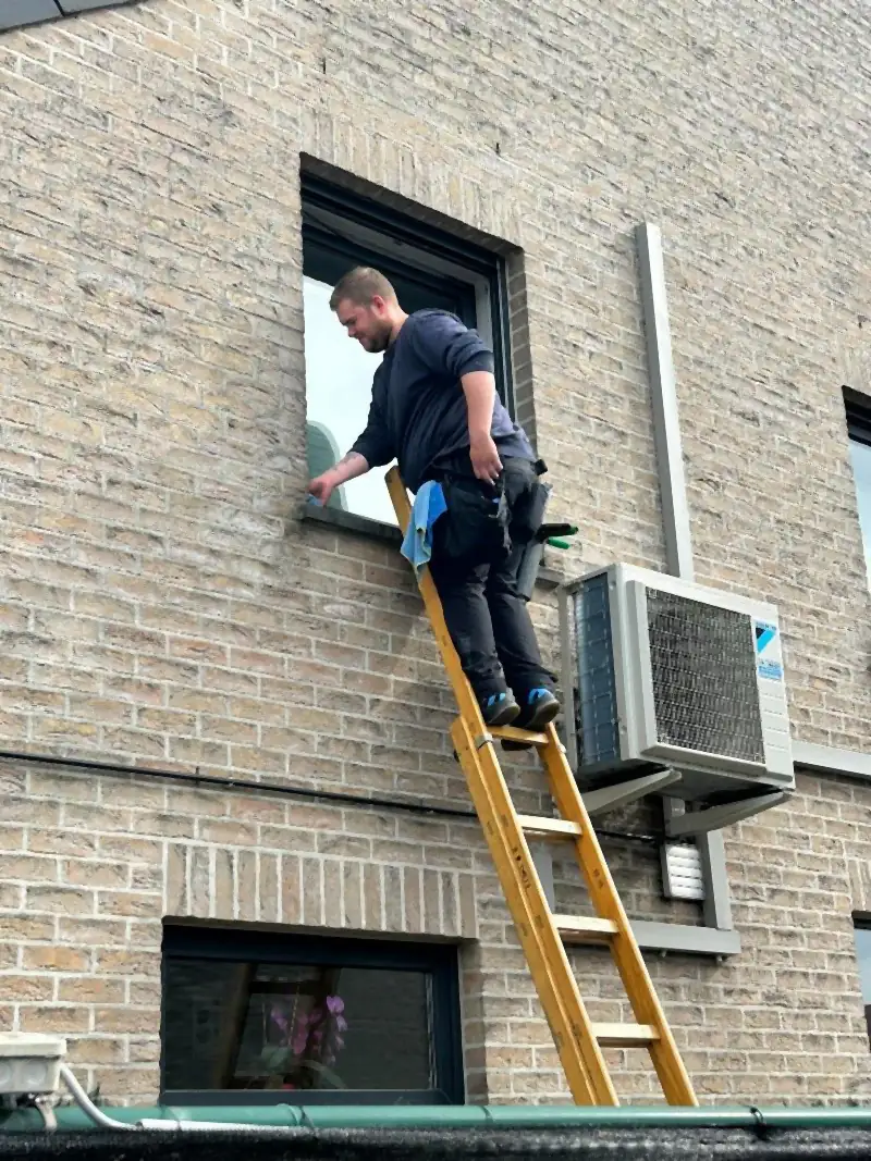 Glazenwasser van Ruitenwasser Smets wast een raam op de eerste verdieping vanop een ladder