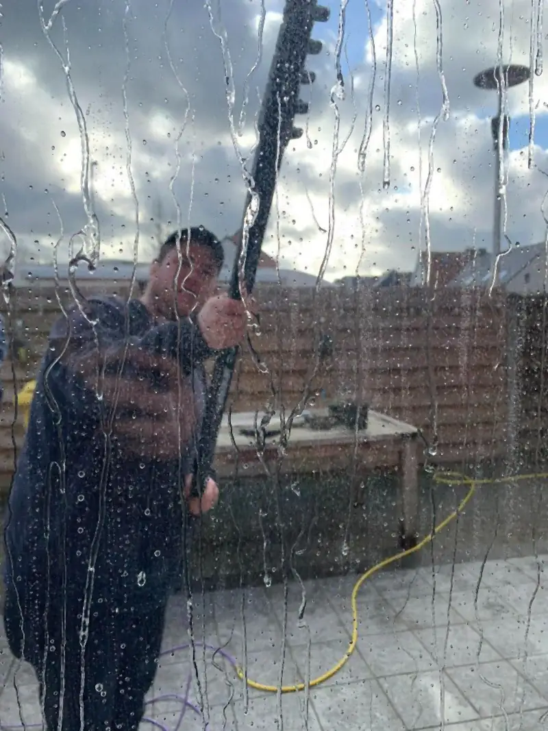 Raam wordt van buiten gewassen met osmosewater en een telescoopsteel, gezien door het natte glas